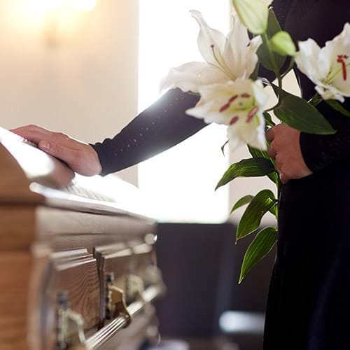 A wood casket and a woman holding white lillies with her hand on the casket