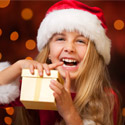 A young child wearing a Santa hat holding a gift and smiling
